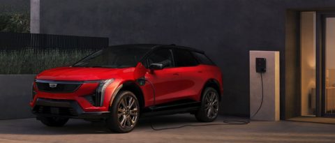 Red Cadillac LYRIQ EV parked and charging at a wall-mounted station outside a modern building.